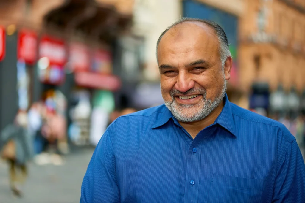 Man smiling at camera wearing blue shirt against a local street background