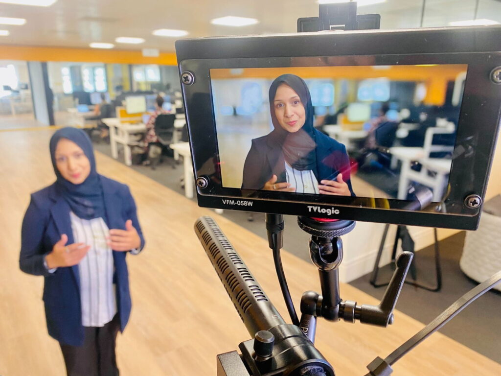 Muslim female journalist talking to the camera in a media studio with her image showing on a screen