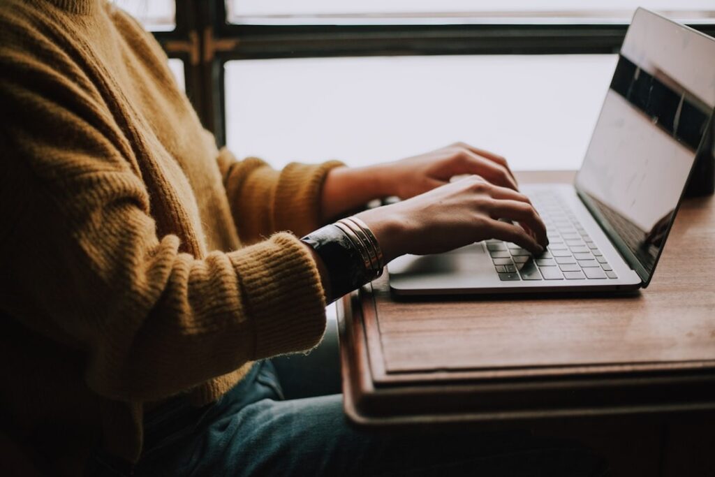 a person typing on a laptop on a wooden table (only body shot, no head showing)