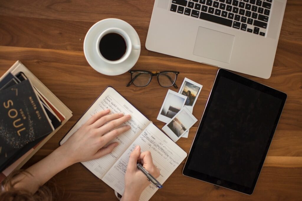 table with laptop, coffee. pictures and book with someone writing into a book